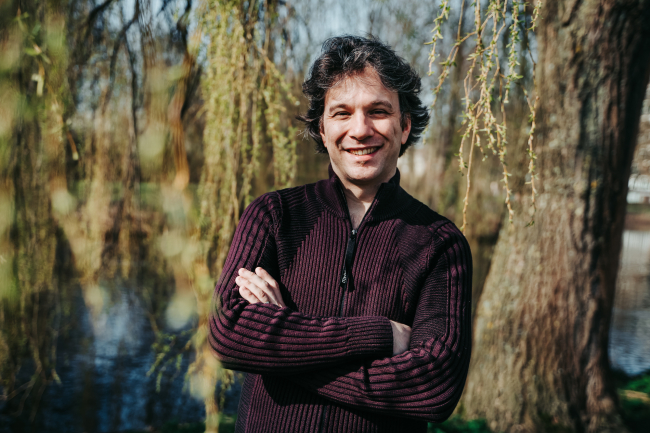 Foto van een man die met gekruisde armen staat, achter hem zijn bomen