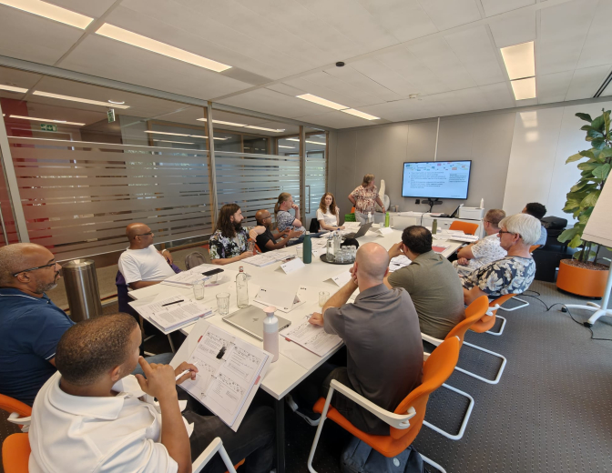 een groep mensen die in een ruimte een training volgen 